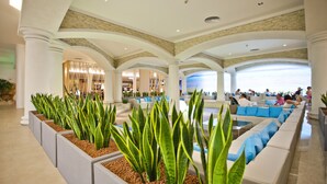 A spacious lobby with a modern design, featuring a seating area with blue cushions, a large plant arrangement, and a view of the lobby area. - DIT Evrika Beach Club Hotel (Nessebar)