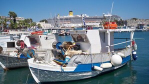 A marina with several boats docked, including a blue and white fishing boat with a cabin and various equipment. - Aegeon Hotel (Kos)