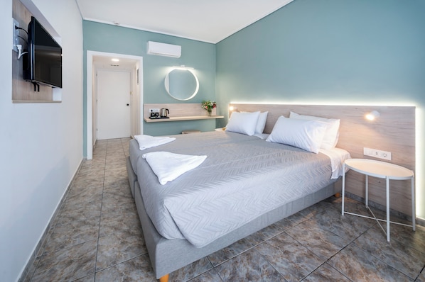 A modern hotel room with a large bed, a bedside table, a TV, and a bathroom with a mirror and sink. - Aegeon Hotel (Kos)