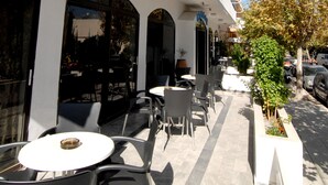 An outdoor cafe area with tables and chairs, a white building facade, and a tree with autumn leaves. - Aegeon Hotel (Kos)