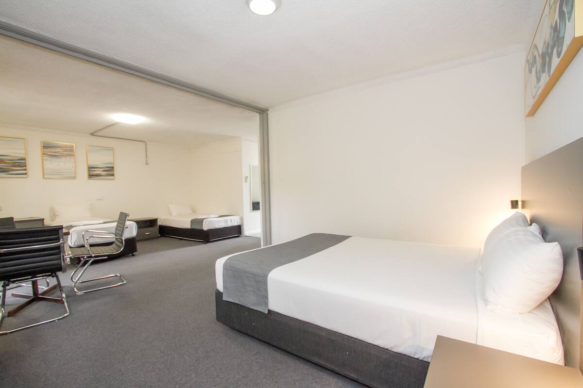 A hotel room with a large bed, a desk, a chair, and a sofa.