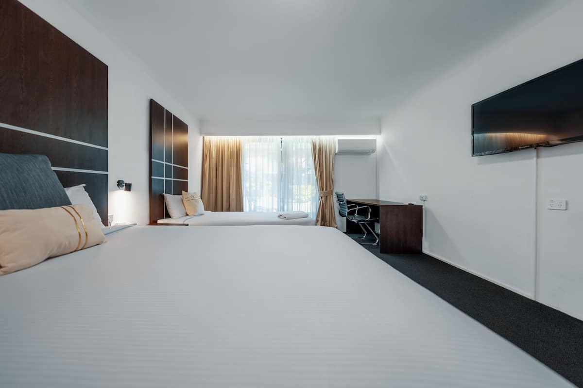 A modern hotel room with a large bed, a desk, and a flat-screen TV mounted on the wall.