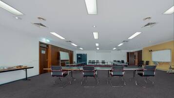 Uma sala de conferências com uma mesa comprida, seis cadeiras, um quadro branco e uma tela de projeção.