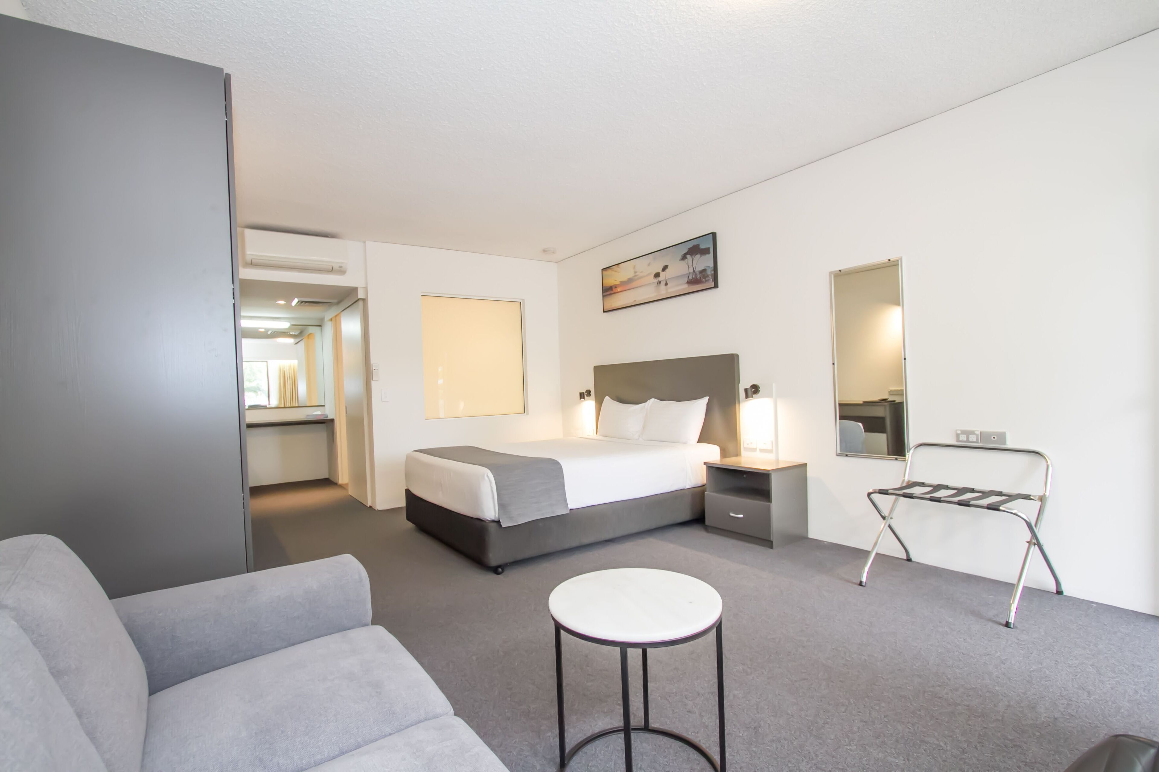 Ett modernt hotellrum med en säng, ett sängbord, en lampa, en stol och ett litet runt bord.