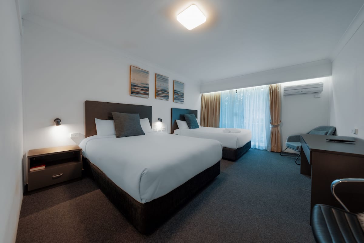 A hotel room with two beds, a desk, and an air conditioning unit.