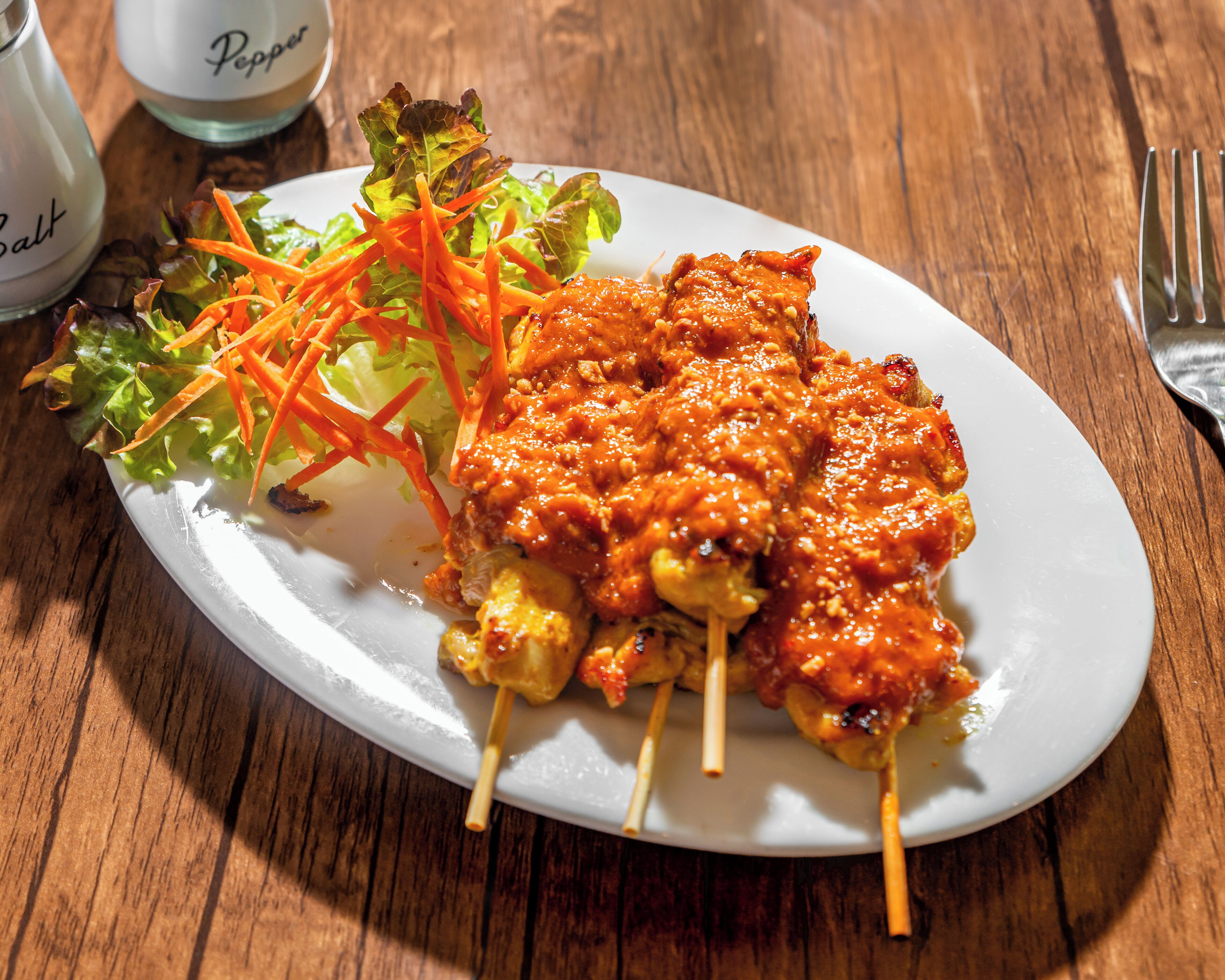 Un plato de brochetas de pollo a la parrilla, acompañadas de una ensalada y salsa para mojar.