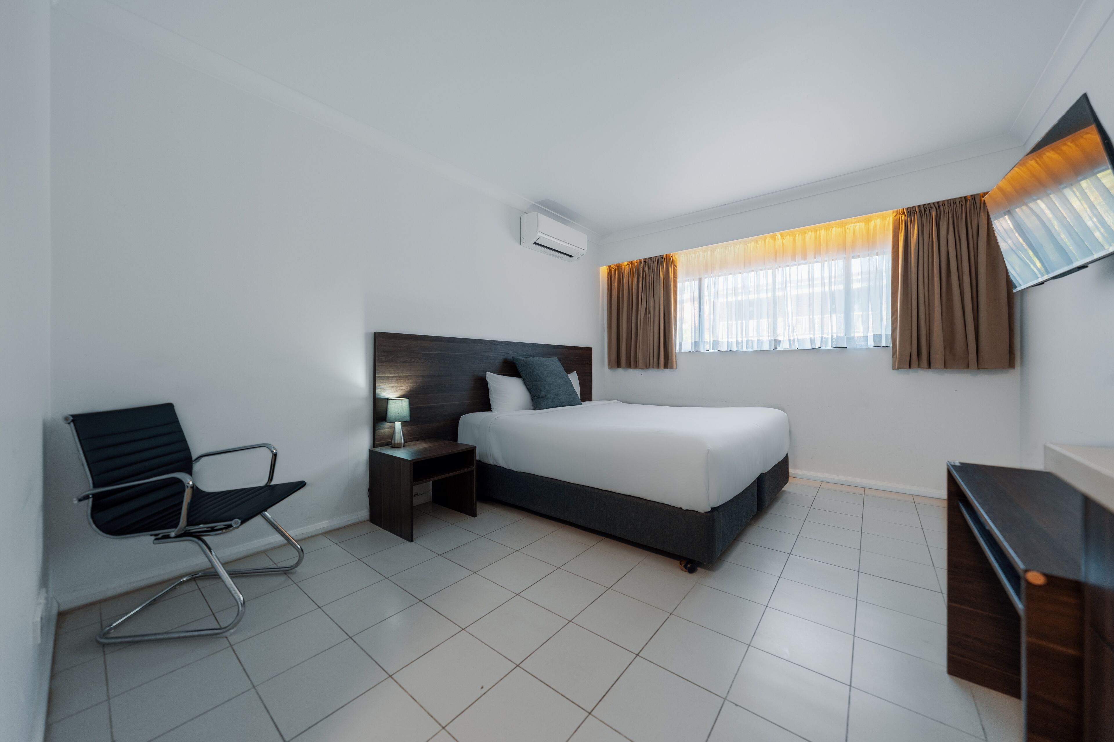 Une chambre d’hôtel moderne équipée d’un lit, d’un bureau, d’une chaise et d’une fenêtre avec des rideaux.