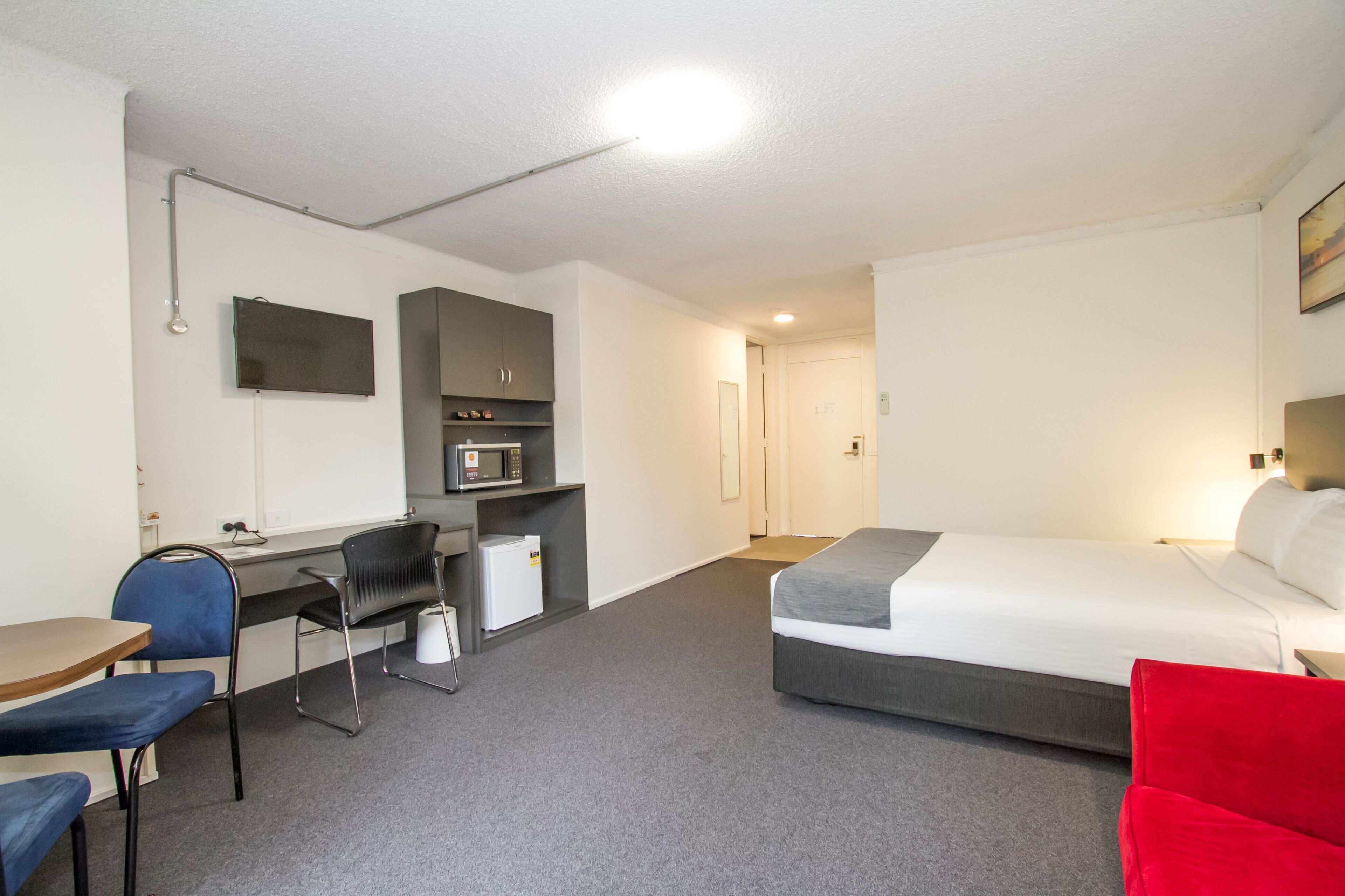 A hotel room with a bed, desk, chair, and a small kitchenette.