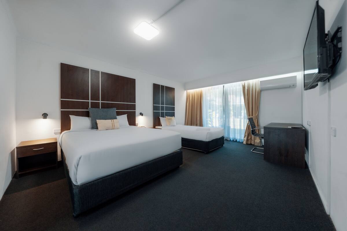 A modern hotel room with two beds, a desk, and a TV mounted on the wall.