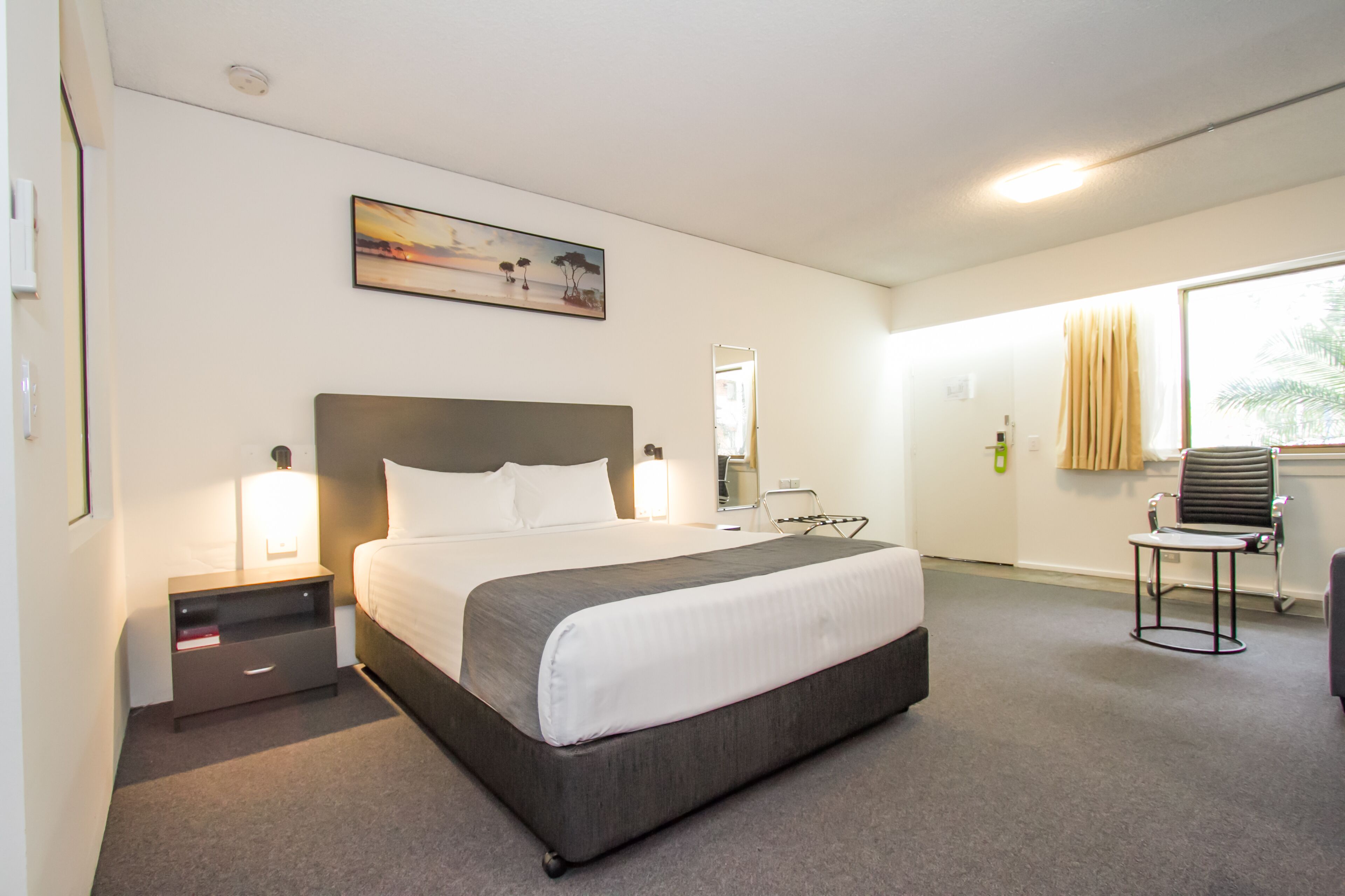 Ein Hotelzimmer mit einem großen Bett, Nachttischen, einem Schreibtisch, einem Stuhl und einem Fenster mit Vorhängen.