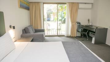 A hotel room with a bed, a sofa, a desk, and a view of the garden through the glass door.