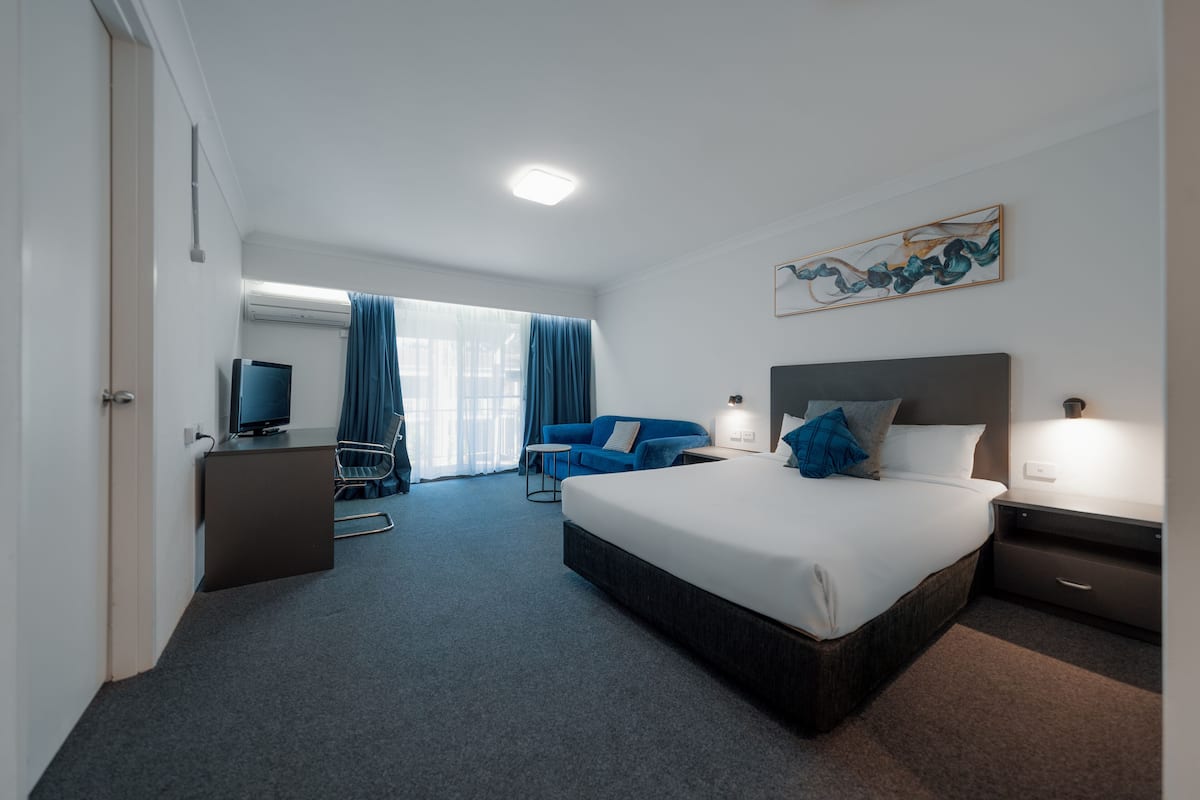 A hotel room with a large bed, a desk with a computer, a sofa, and a TV.