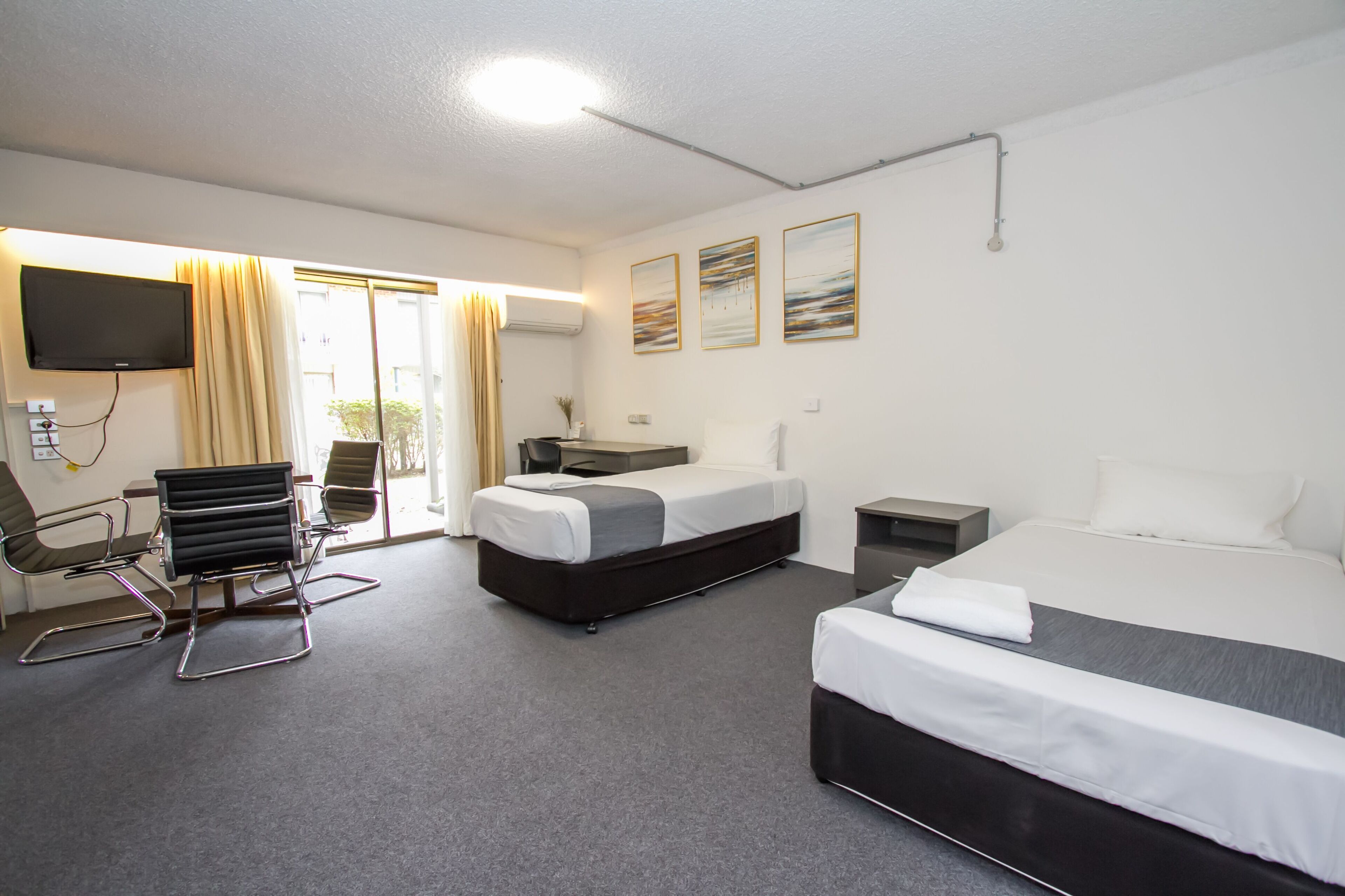Una habitación de hotel con cama, escritorio, silla, televisor y ventana con cortinas.