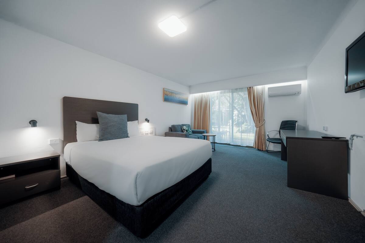 A hotel room with a large bed, bedside tables, a desk, a chair, and a TV on the wall.