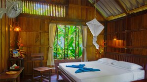 A wooden room with a bed, a fan, a table with a basket, and a chair.