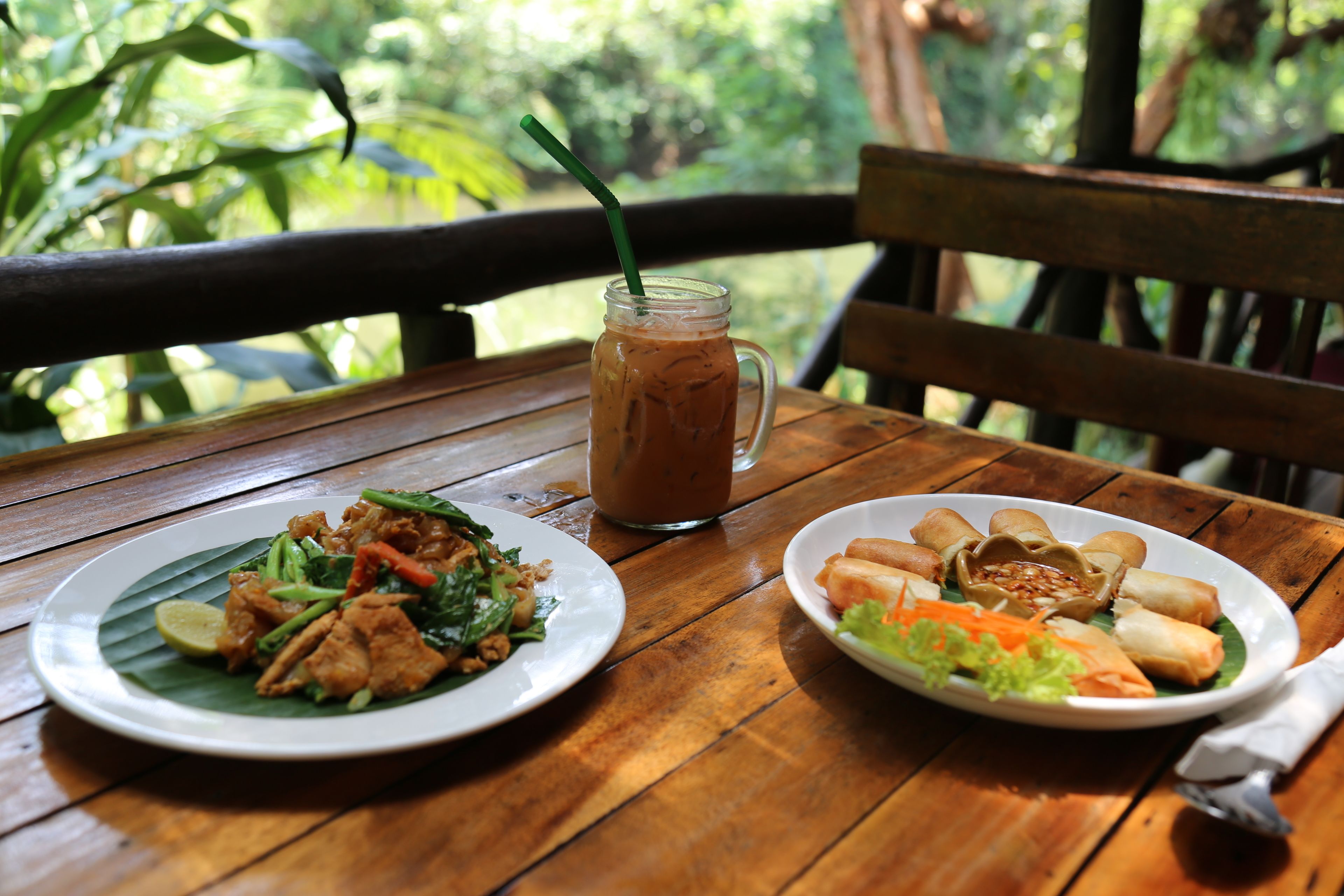 A wooden table with two plates of food and a glass of iced tea.