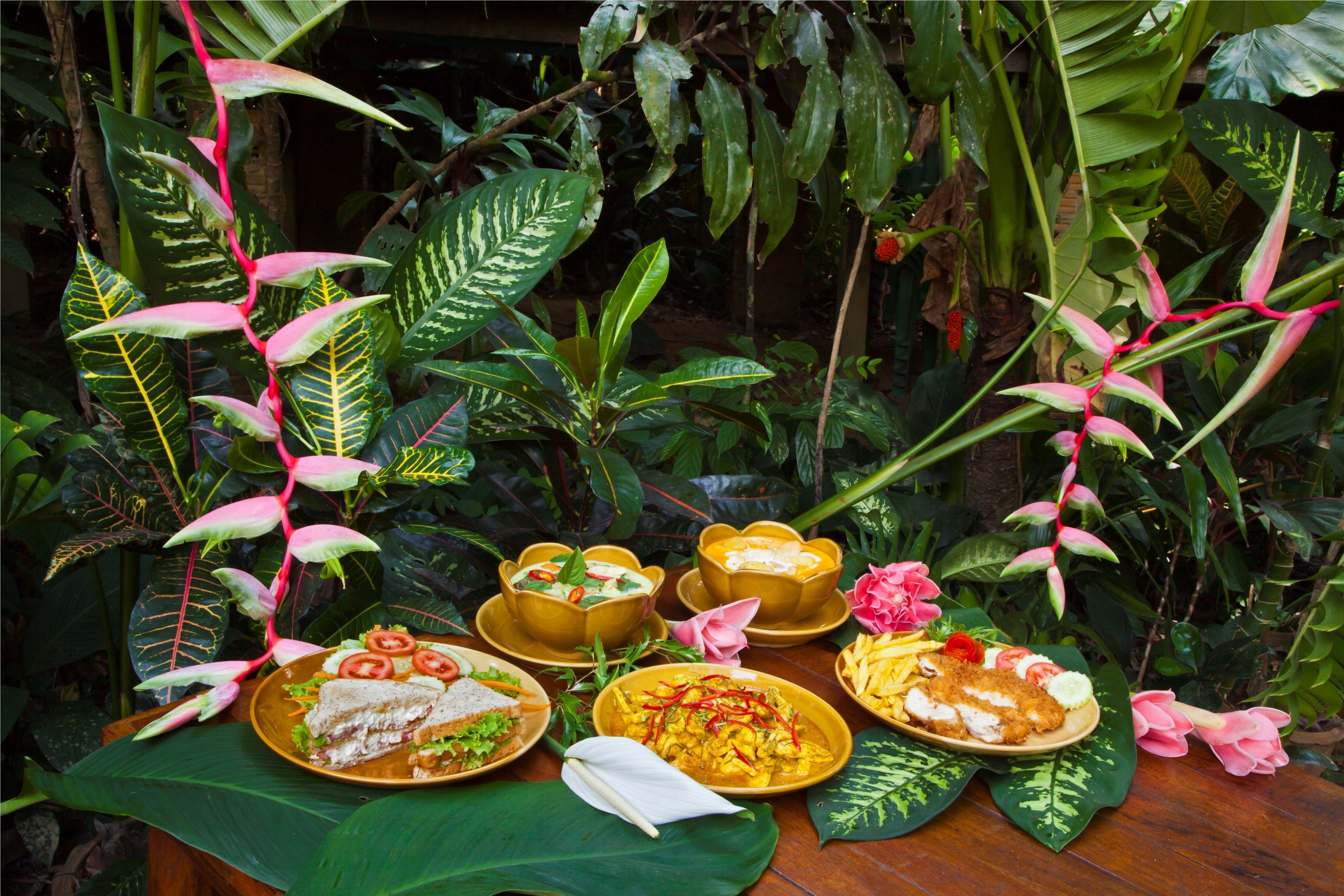 A table set with various dishes in a lush, green environment.