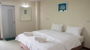 Un lit bien fait, avec du linge de lit blanc et deux serviettes enroulées, une porte dotée d’une grille d’aération et un tableau encadré accroché au mur.
