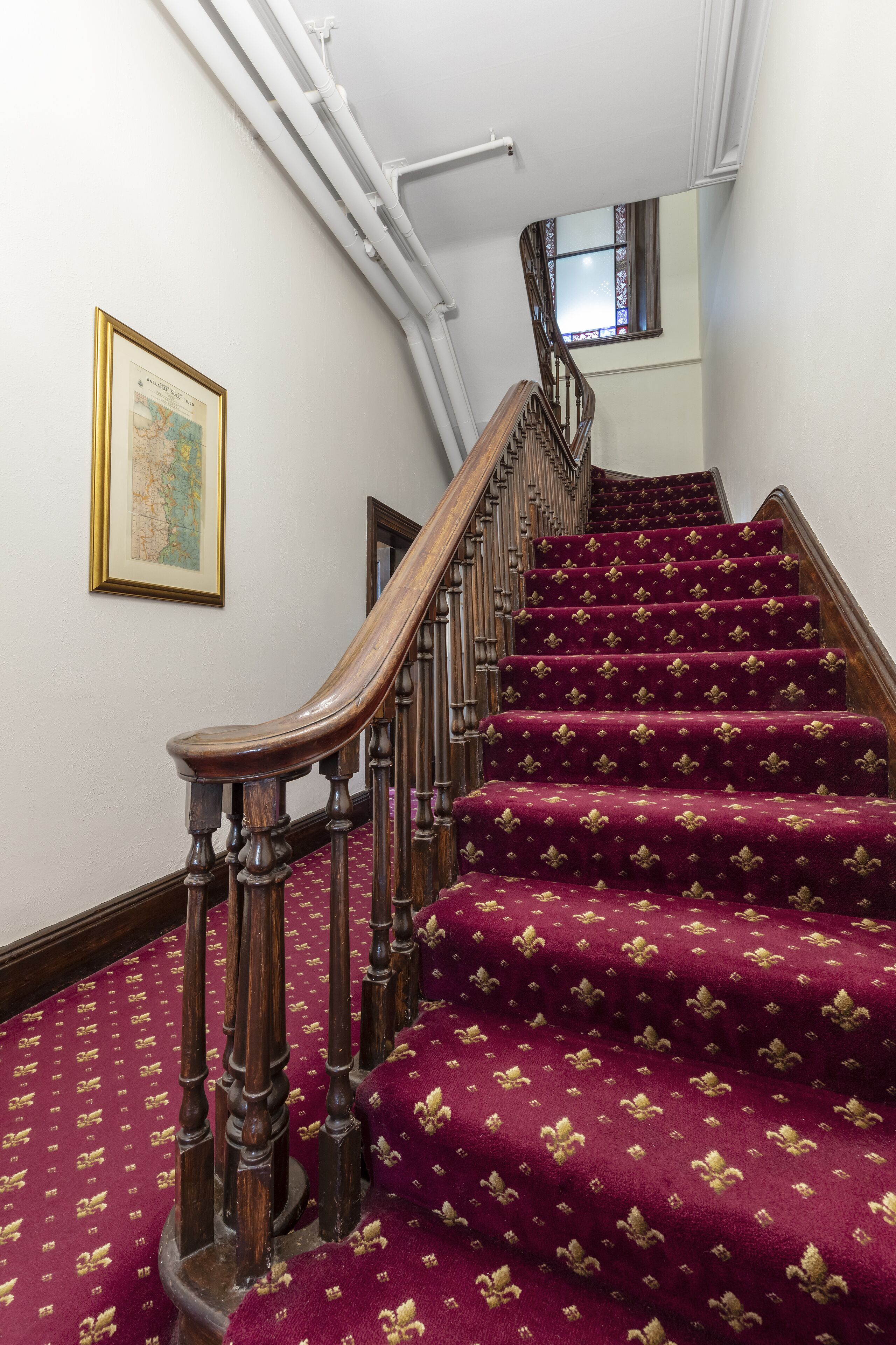 Una escalera con barandilla de madera y peldaños alfombrados de color rojo.