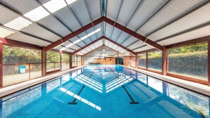 Una piscina interior con carriles delimitados, rodeada por amplios ventanales y una estructura de techo metálico.
