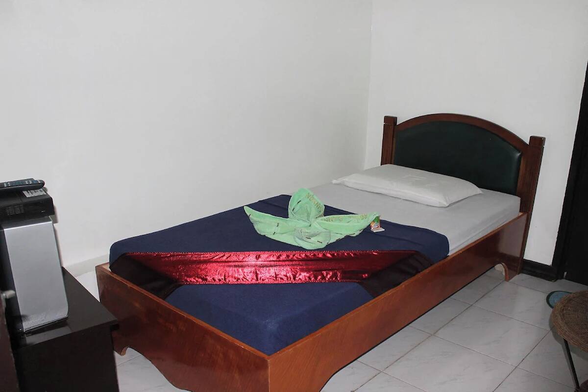 A single bed with a wooden frame, a blue mattress, and a green cloth on the bed.