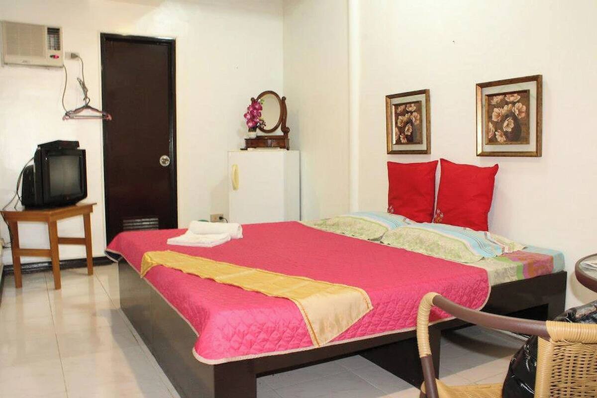 A bedroom with a bed, a television on a stand, a door, and two framed pictures on the wall.