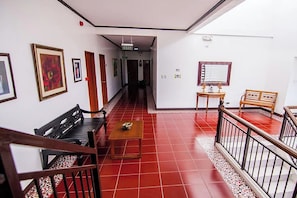 Un pasillo con suelo de baldosas rojas, bancos de madera, una mesita y un espejo en la pared.