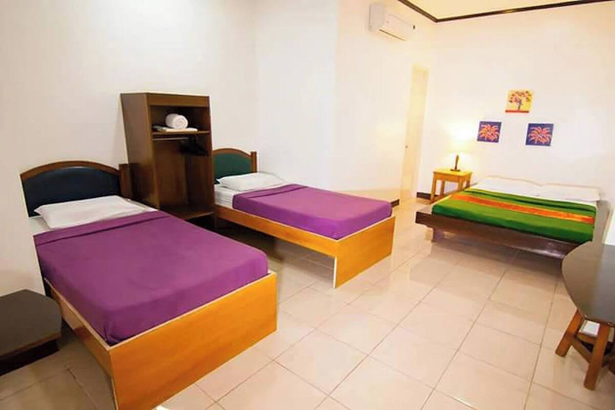 A room with two single beds, a wooden wardrobe, a small table with a lamp, and a chair.