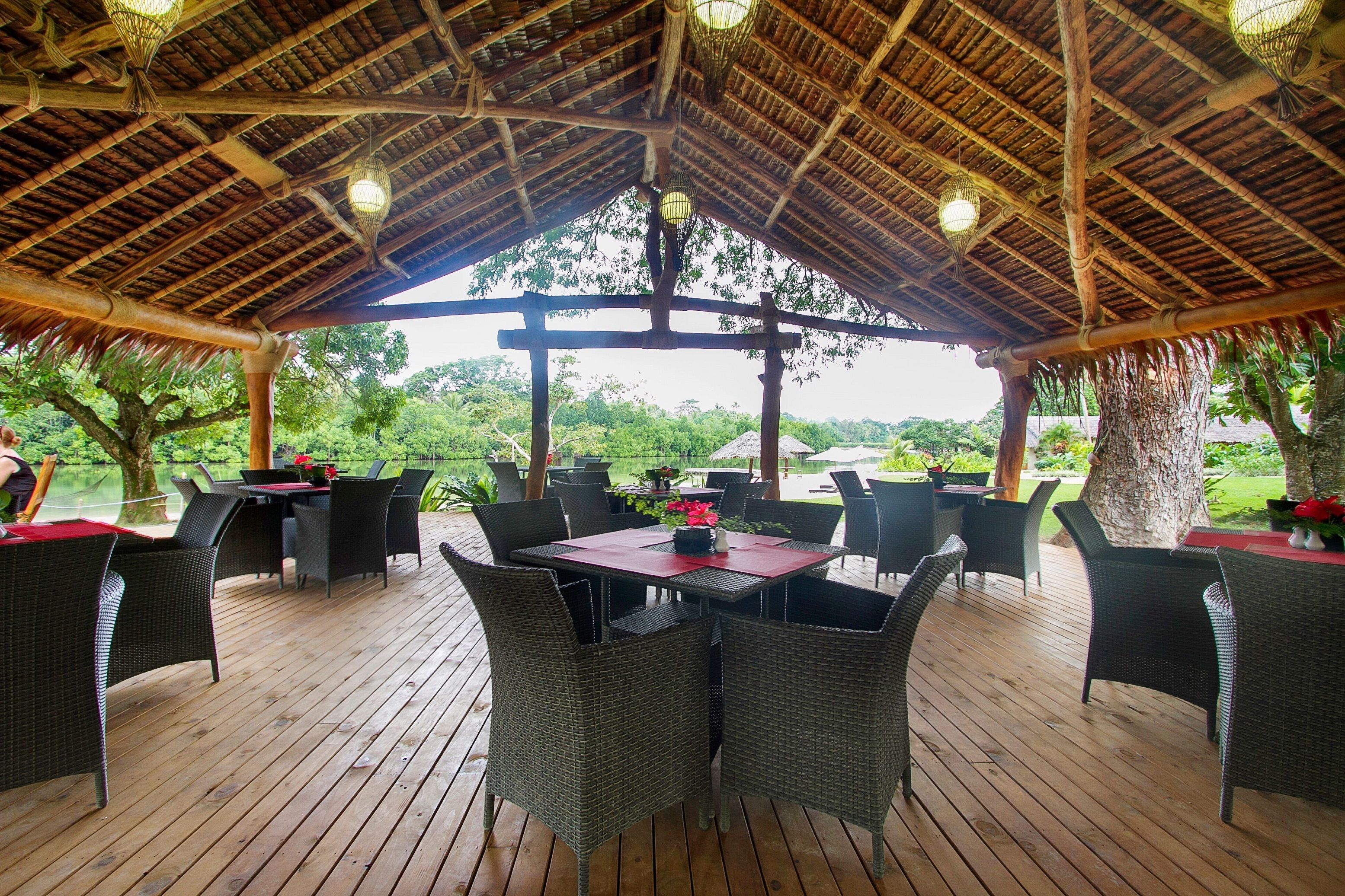 An outdoor covered patio with wicker furniture, a central table with a red tablecloth, and hanging lights.