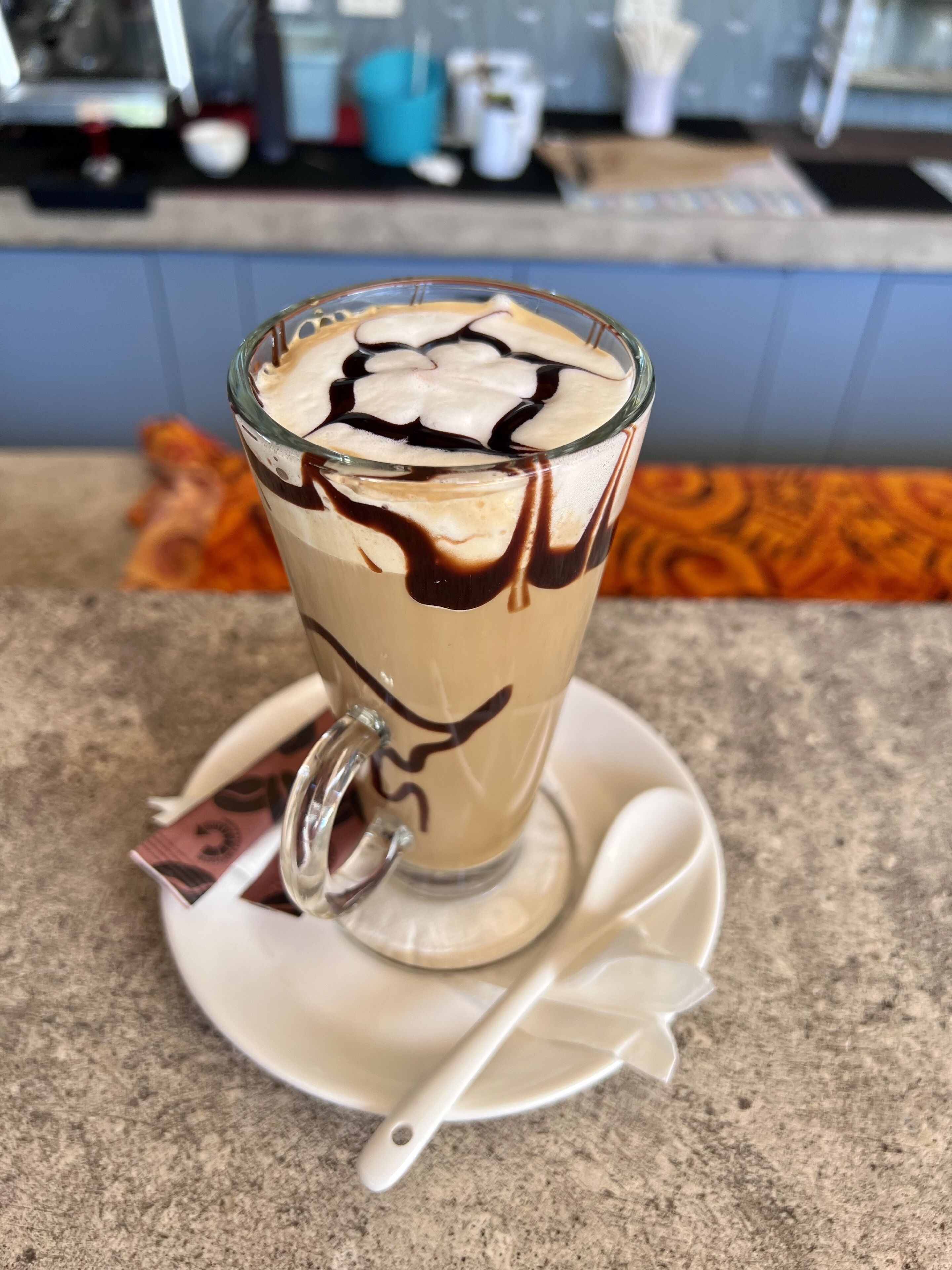 A glass of iced coffee with chocolate syrup on a white saucer.