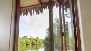 A sliding glass door leading to a beach with a view of a calm lake and greenery. - MG Cocomo Resort Vanuatu (Port Vila)