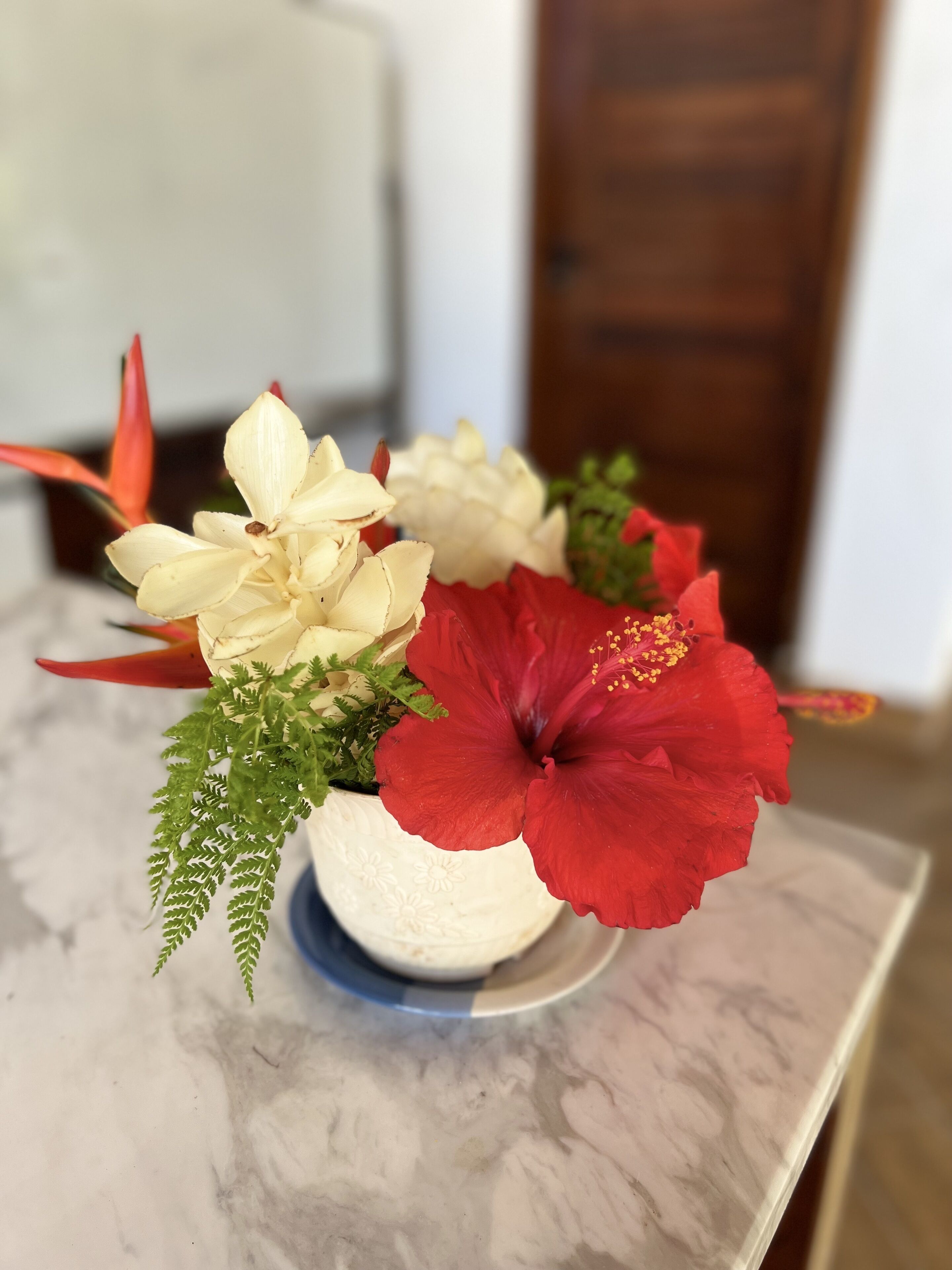 A marble table with a white ceramic pot containing a floral arrangement of white and red flowers, green foliage, and red leaves.