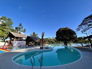 A swimming pool with a thatched-roof structure and a rainbow slide nearby.