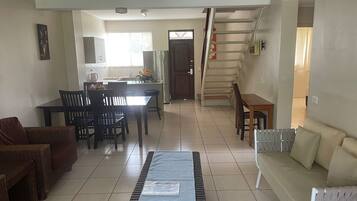 A spacious living area with a dining table, chairs, a sofa, and a staircase leading to an upper floor.