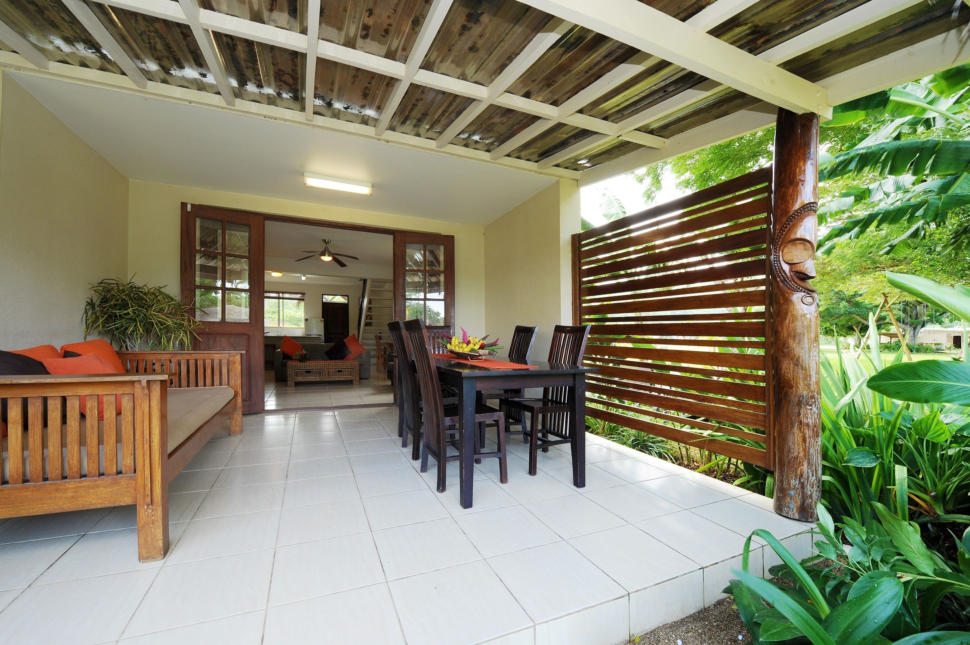 Ein überdachter Patio-Bereich mit Holztisch und -stühlen, einer Bank und Blick auf üppiges Grün.