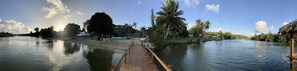 A wooden bridge over a calm river, surrounded by lush greenery and palm trees.