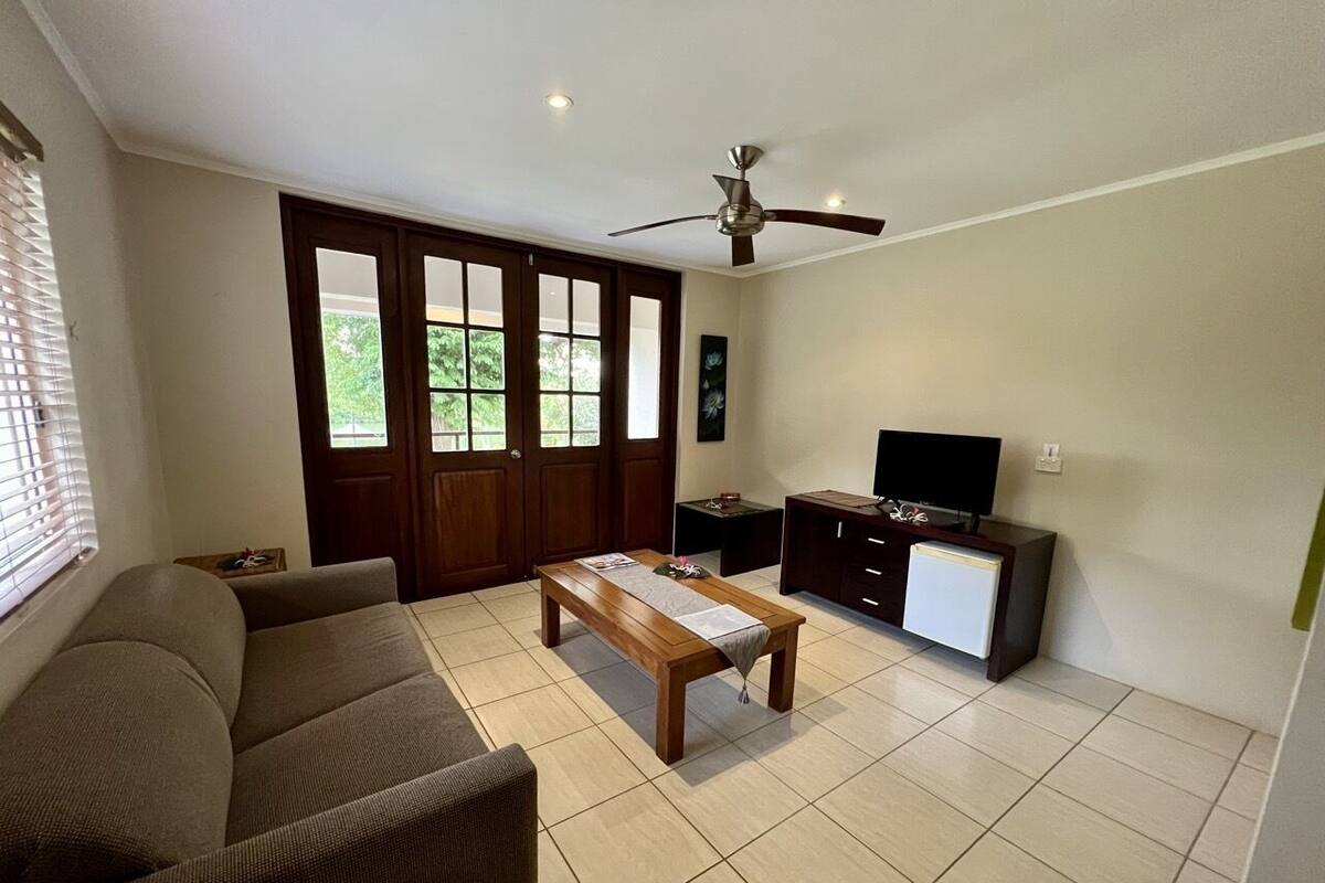 Ein Wohnzimmer mit einer Couch, einem Holztisch, einem Fernsehschrank und einem Deckenventilator.