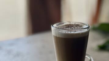 A tall glass of layered beverage on a saucer with a spoon, placed on a table.