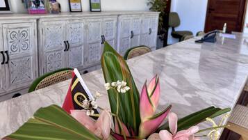 Una mesa de mármol con un centro de mesa floral, un aparador blanco con puertas decorativas y diplomas enmarcados en la pared.