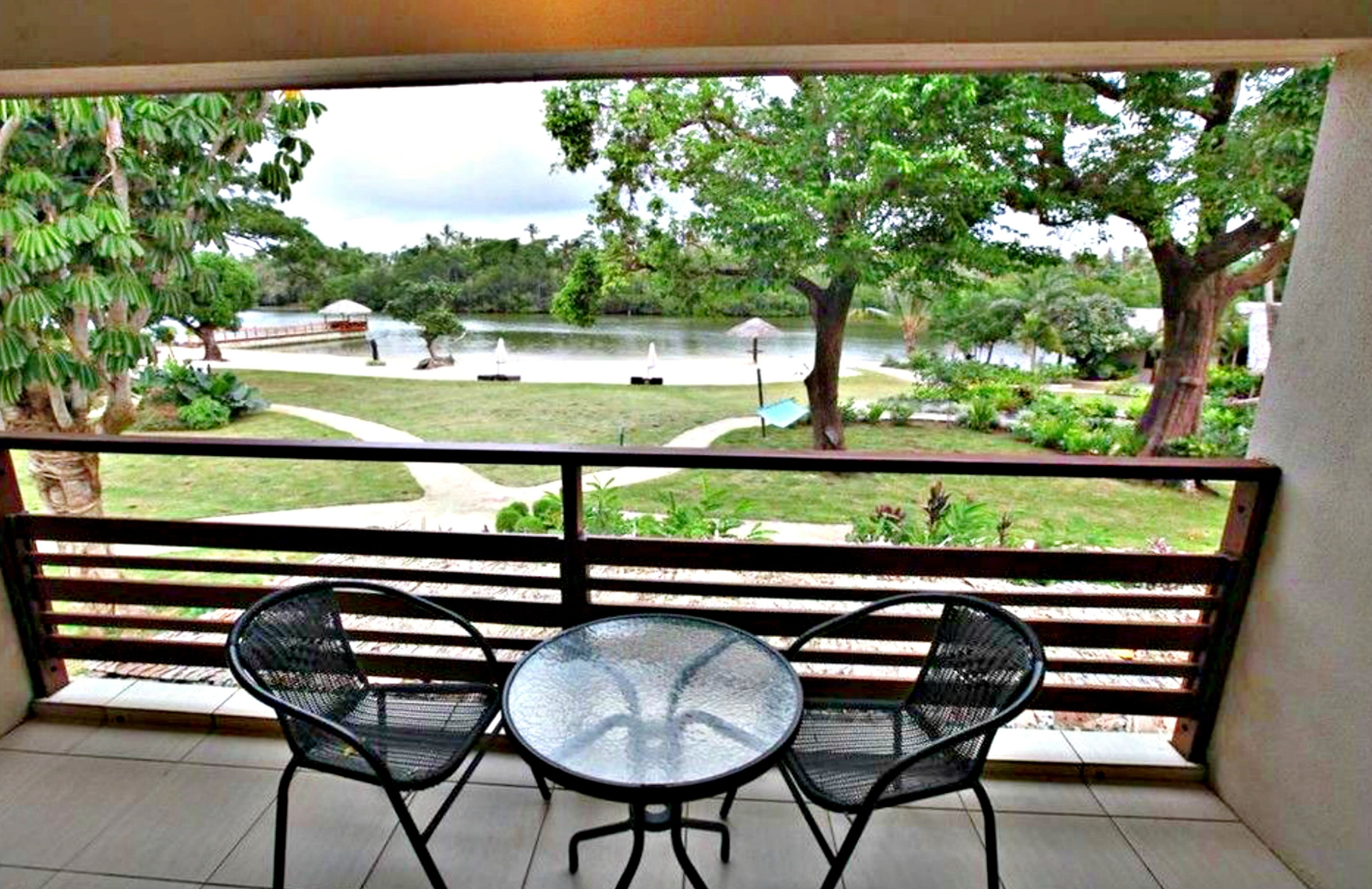 Un balcón con dos sillas y una mesa, con vista a un lago con barcos y vegetación exuberante.