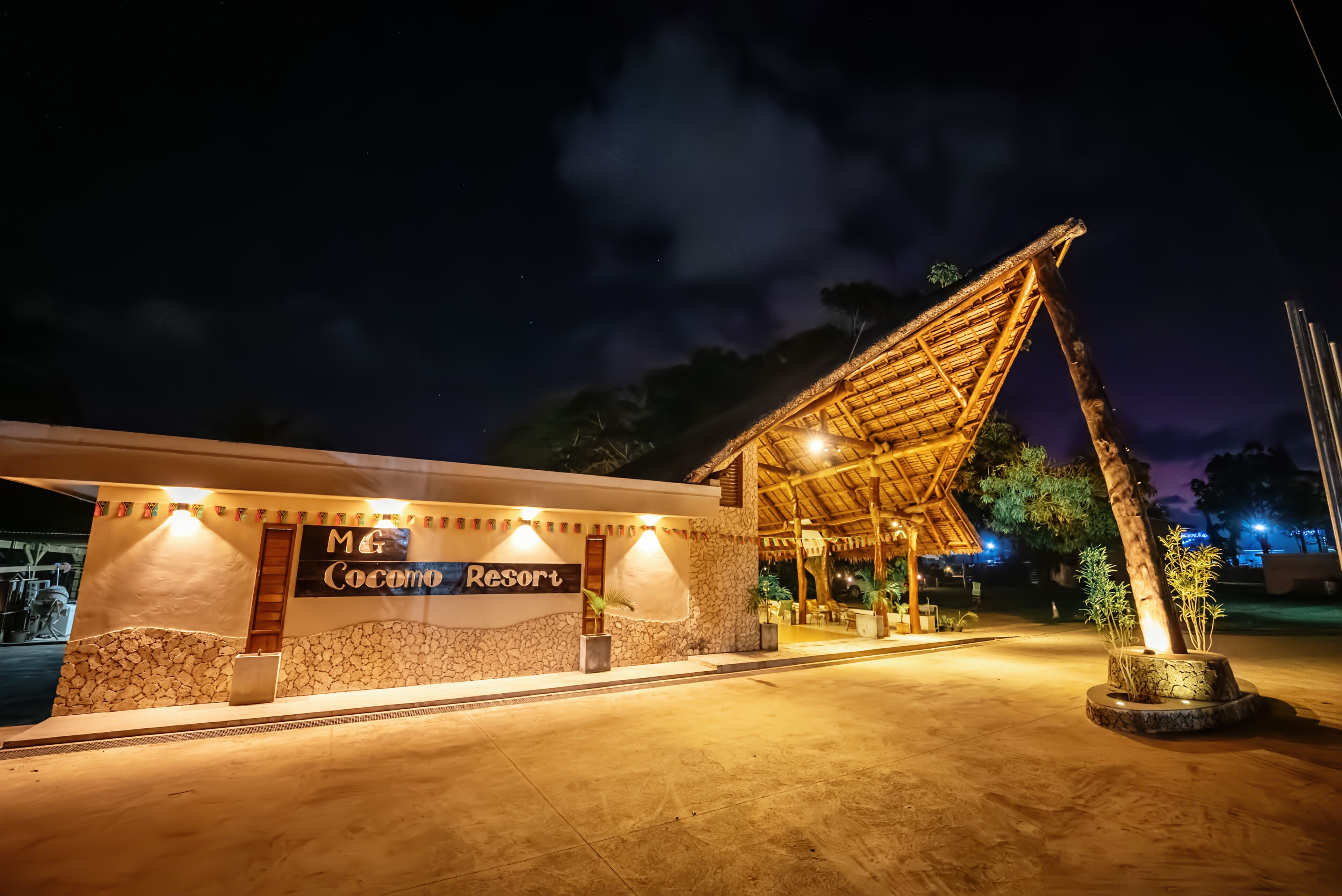 L'ingresso di un resort con facciata in pietra, un cartello che recita "M & Coconu Resort" e una struttura con tetto di paglia.