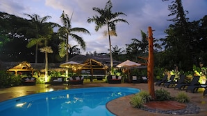 A pool area with lounge chairs and umbrellas, surrounded by palm trees and a thatched-roof structure. - MG Cocomo Resort Vanuatu (Port Vila)