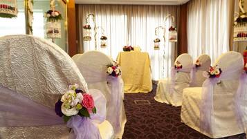 A room with white chairs covered in sheer fabric and floral arrangements, a yellow table, and hanging decorations.