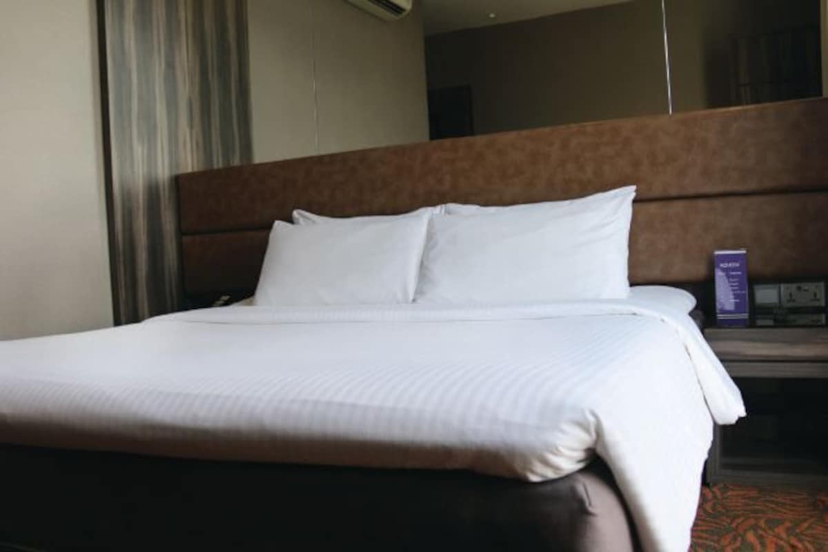 A hotel room with a large bed, a wooden headboard, a nightstand with a lamp, and a mirror on the wall.