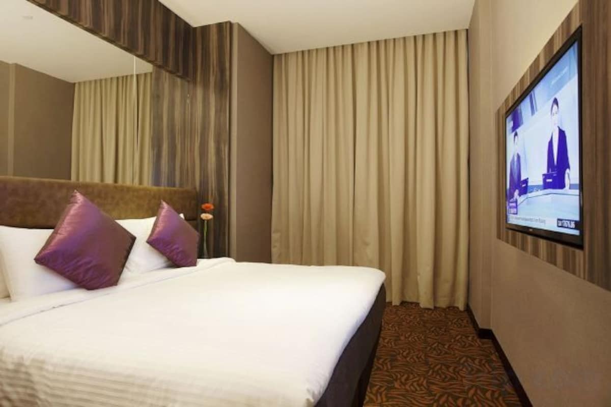 Une chambre d’hôtel avec un lit, un téléviseur fixé au mur et un rideau.