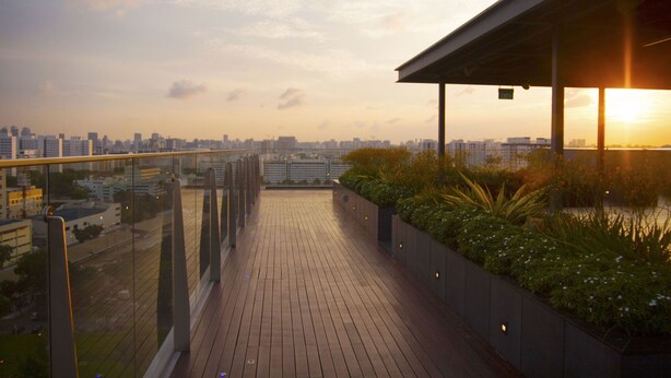 Eine Dachterrasse mit Blick auf die Stadt, Holzboden und eine Glasreling.