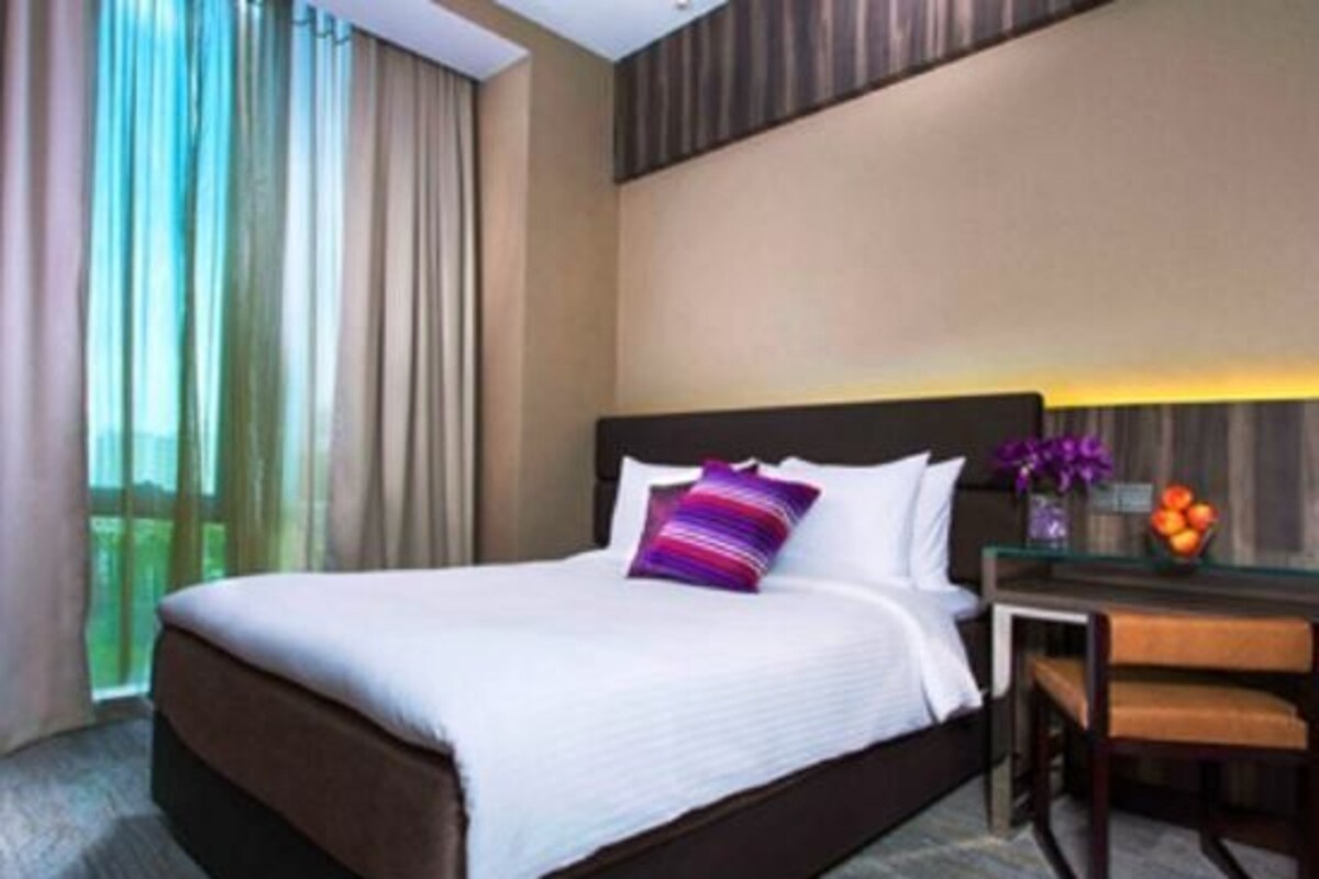 Habitación de hotel con una cama grande, una mesita de noche, una silla y vistas al exterior.