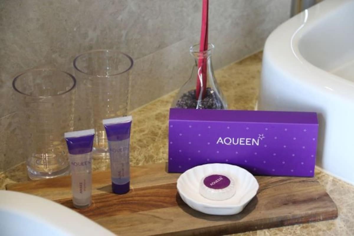 Un tocador de baño con artículos de aseo, una caja morada etiquetada 'AQUEEN' y un lavabo blanco.