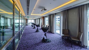 Ein Hotelkorridor mit violettem, gemustertem Teppich, Glaswänden und einer Sitzecke mit Stühlen und Tischen.