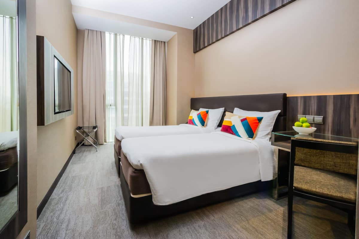 Una habitació d'hotel amb dos llits, un televisor de pantalla plana, una taula de vidre amb un bol de fruita i una finestra gran amb cortines.
